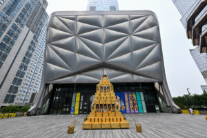 The ridged steel shell of The Shed at Hudson Yards, with a tiered gold sculpture standing on the plaza in front of the entrance