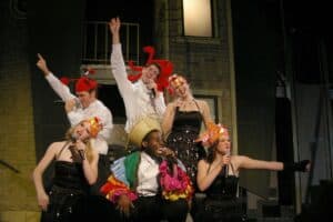 Group of actors performing on stage in costumes, celebrating with microphones.