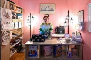 Person at NYC map-themed merchandise store counter with books and souvenirs.