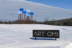Snow-covered landscape with Omi Art Park sculpture and sign in New York State.