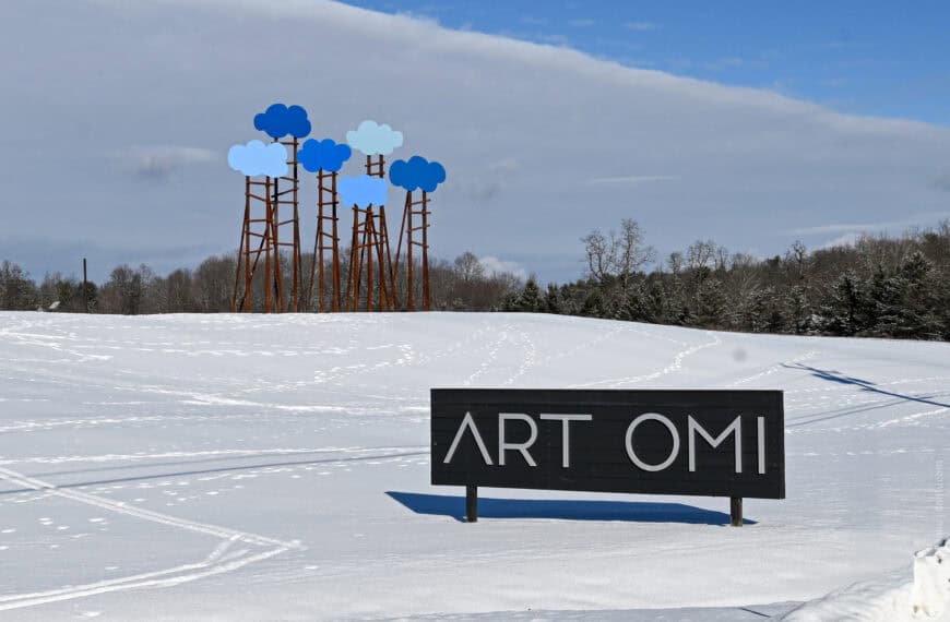 Snow-covered landscape with Omi Art Park sculpture and sign in New York State.