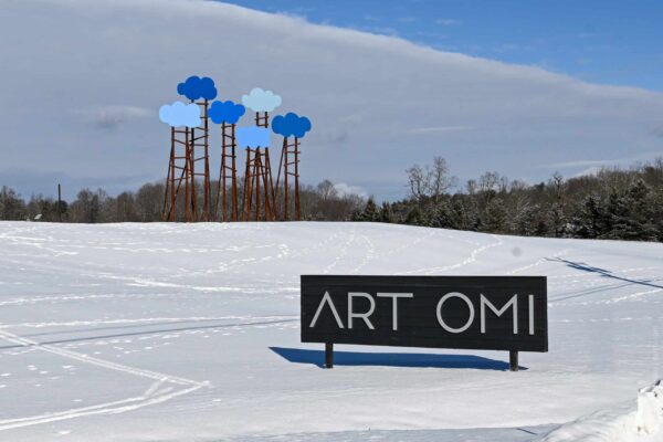 Snow-covered landscape with Omi Art Park sculpture and sign in New York State.