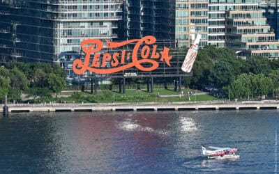 Pepsi-Cola neon sign on Manhattan waterfront with city buildings in background.