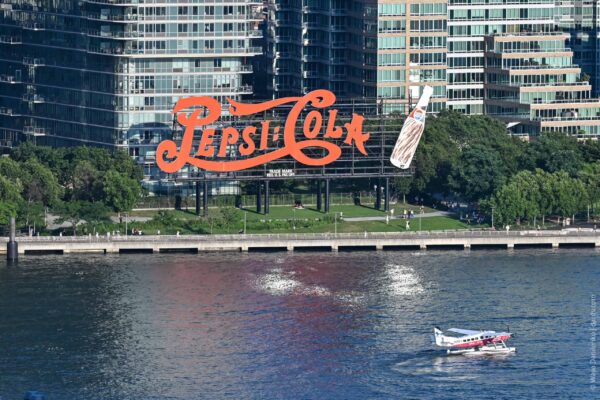 Pepsi-Cola neon sign on Manhattan waterfront with city buildings in background.