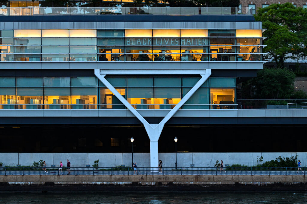 Laboratory windows of the Kravis Research Building at Rockefeller University spelling out BLACK LIVES MATTER in taped letters, above the East River esplanade at dusk